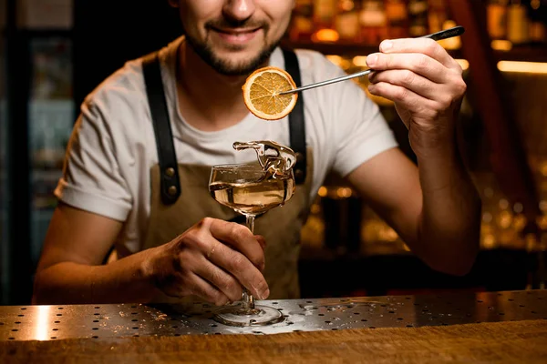 Barista maschio che aggiunge a un cocktail alcolico una fetta di limone essiccata con pinzette — Foto Stock
