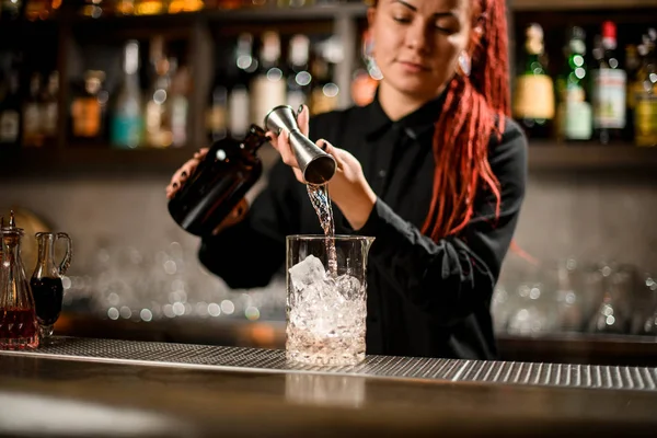 Garota barman derramando uma bebida alcoólica do jigger para um copo de vidro de medição — Fotografia de Stock