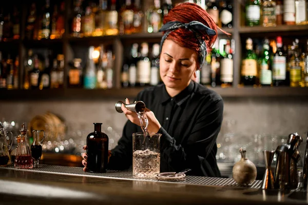 Barman meisje met een rood haar gieten van een alcoholische drank van het jigger naar een maatglas beker — Stockfoto