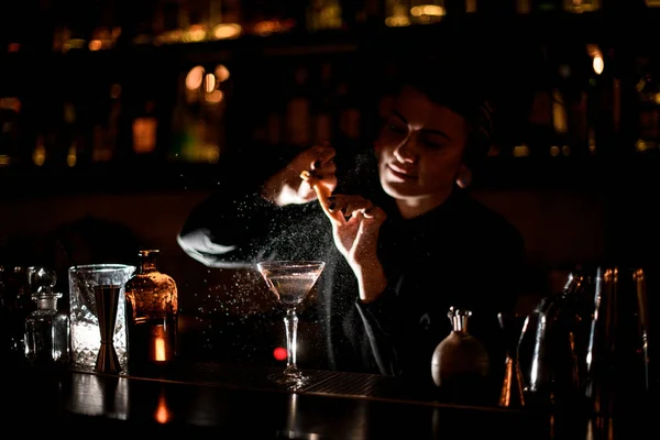 Bartender girl sprinkling on a alcoholic drink in the cocktail glass with a orange zest juice — Stock Photo, Image