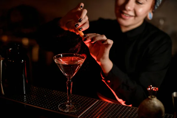 Garota de barman sorridente polvilhando em uma bebida alcoólica no copo de coquetel com um suco de raspas de laranja — Fotografia de Stock