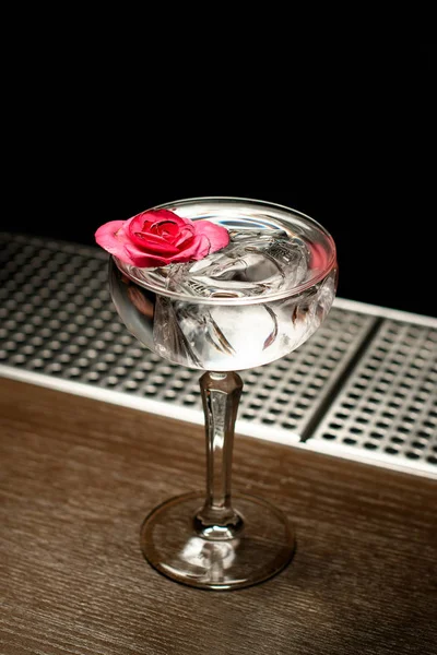 Cóctel alcohólico transparente con hielo en el vaso decorado con un capullo rosa — Foto de Stock