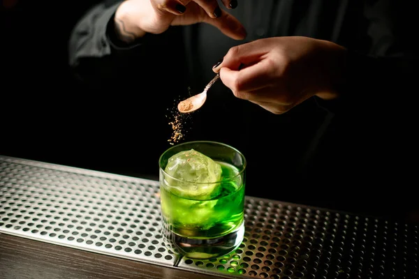 Barman girl servant un cocktail alcoolisé vert dans le verre en ajoutant des épices de la petite cuillère — Photo