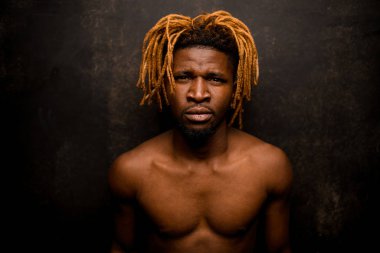 Stüdyoda fotoğraf makinesine bakan sarışın, siyah, çıplak bir adam.