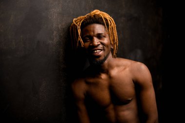 Gülümseyen Afro-Amerikan adam çıplak göğsüyle poz veriyor.