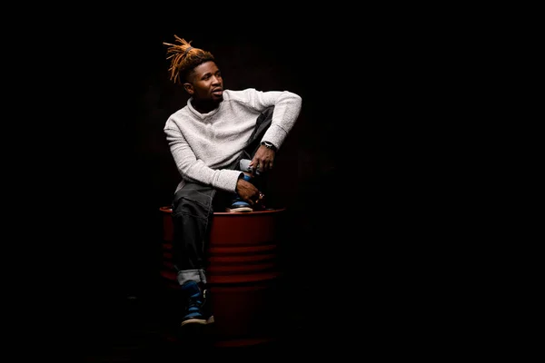 Hombre negro con rastas rubias posando en cuclillas en el barril de petróleo —  Fotos de Stock