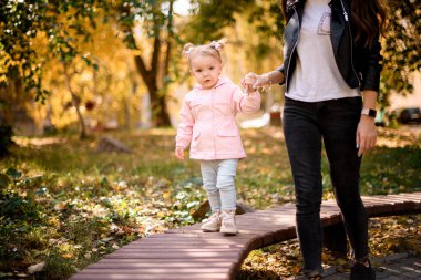 Küçük kızının elini tutan genç anne bankta yürümeye yardım ediyor.