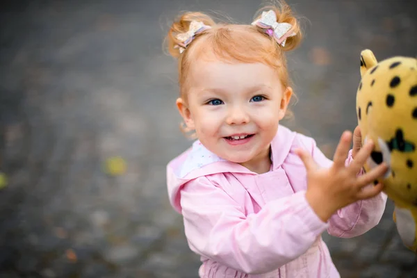 Usmívající se holčička stojící v podzimním parku se žlutou černou tečkovanou hračkou v rukou — Stock fotografie