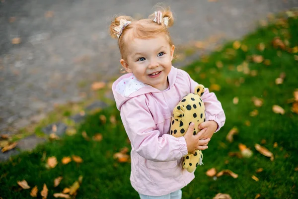 Niña sonriente de pie en el parque de otoño abrazando un juguete punteado negro amarillo — Foto de Stock