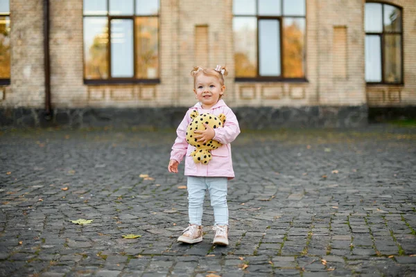 Menina de pé na rua abraçando um brinquedo pontilhado preto amarelo — Fotografia de Stock