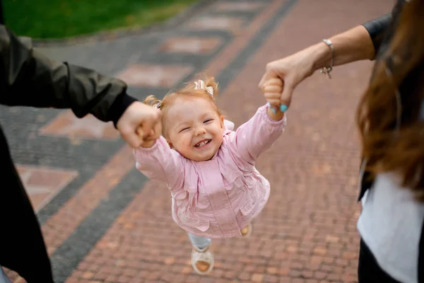 Mãe e pai carregando sua filha segurando as mãos no parque — Fotografia de Stock