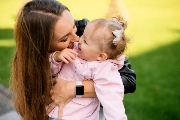 Mother hugging her daughter holding in the armn touching noses — Stock Photo, Image