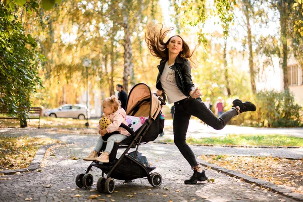 Vrolijke moeder springen omhoog met een haar dochter kinderwagen — Stockfoto