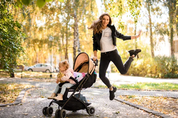 Happy mother jumping up holding a her daughter baby carriage — Stock Photo, Image