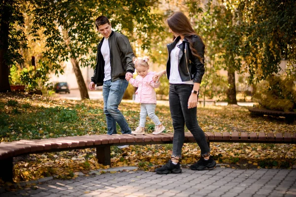 Moeder en vader houden hun dochtertje vast en helpen op de bank te lopen. — Stockfoto