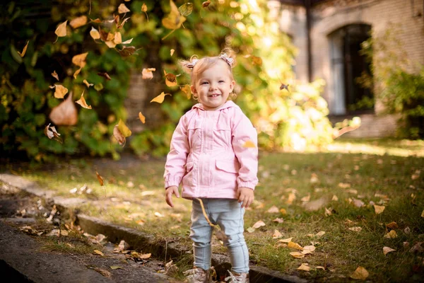 Sorrindo menina brincando com amarelo caído folhas de pé na fronteira — Fotografia de Stock