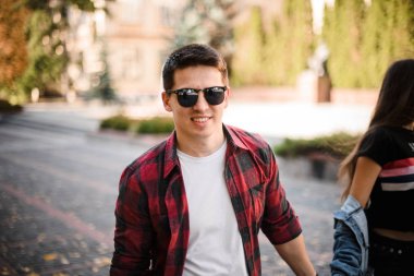 Adam sonbahar parkında karısının elini tutarak parkta yürüyor.