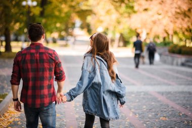 Sonbahar parkında el ele tutuşan romantik bir çift.