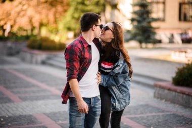 Sonbahar parkında el ele tutuşup öpüşen romantik çift.