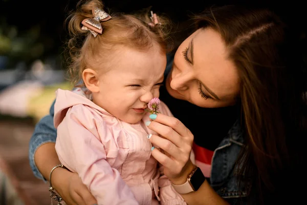 Mère jouant avec sa fille lui donnant l'odeur de la fleur dans le parc — Photo