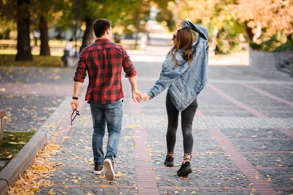 Rear view romantic couple walking in the autumn park holding hands — Stock Photo, Image