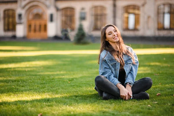 Porträtt av en ung kvinna som sitter på det gröna gräset i höstparken — Stockfoto