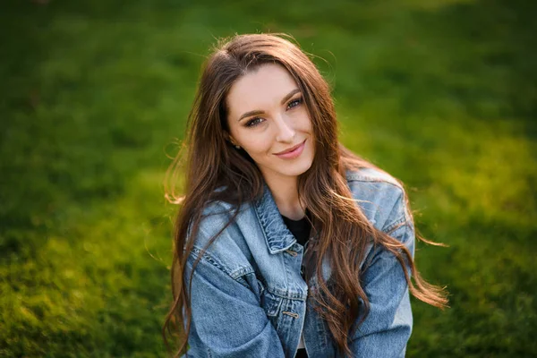 Portret van een mooie vrouw zittend op het groene gras in het herfstpark — Stockfoto