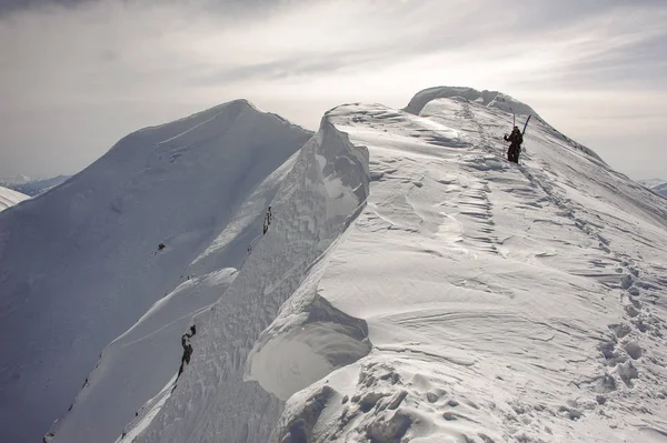 Narciarze ze sprzętem narciarskim schodzą w dół góry — Zdjęcie stockowe