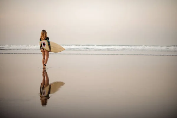 リアビュー女の子でザ黒ダイビングスーツ歩くと海に海岸でサーフボード — ストック写真