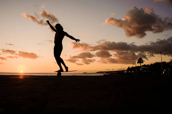 Silueta del hombre de pie en el tablero de equilibrio en la orilla del océano en una pierna —  Fotos de Stock