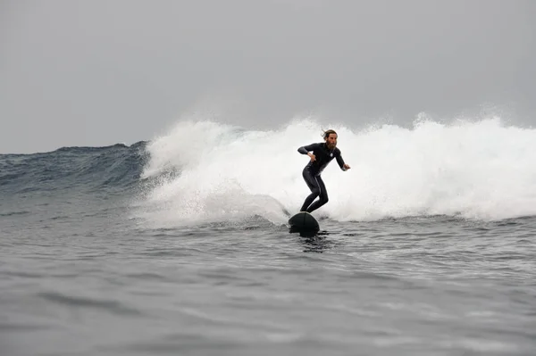 Mannen i svart dykardräkt med skägg ridande på surfing — Stockfoto