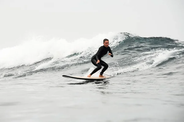 Mujer en el traje de buceo negro cabalgando en la tabla de surf en las rodillas de flexión — Foto de Stock