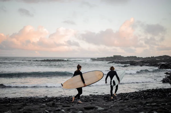 Dois surfistas homens e mulheres com as pranchas de surf andando na costa do mar — Fotografia de Stock