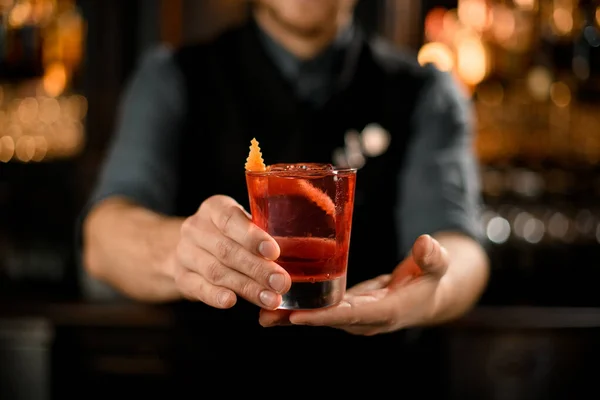 Barman drží alkoholický nápoj s pomerančovou kůrou — Stock fotografie