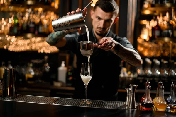Bartender cooks cocktail with shaker and sieve