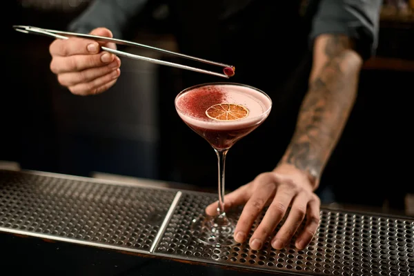 Barkeeper dekoriert einen alkoholischen Cocktail im Glas mit einer getrockneten Orange und roten Gewürzen mit einer Pinzette mit Rosenblüte — Stockfoto