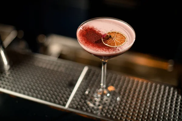 Cocktail rosso decorato con fetta di arancia essiccata, spezie rosse e bocciolo di rosa poco essiccato — Foto Stock