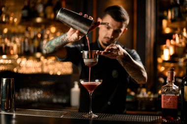Profesyonel erkek barmen, alkollü bir içeceği çelikten bardağa elek yoluyla dolduruyor.