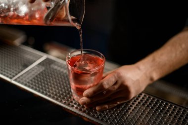 Barmen ölçü kabından süzgeç filtresinden bardağa alkollü bir içecek dolduruyor.