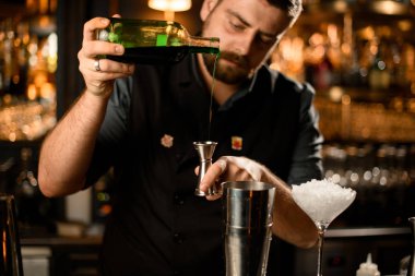 Erkek barmen cam şişeden çeliğe yeşil bir içki dolduruyor.