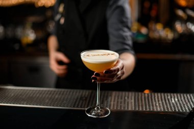 Barmen kız beyaz bir pislikle sarı alkollü kokteyl servisi yapıyor.