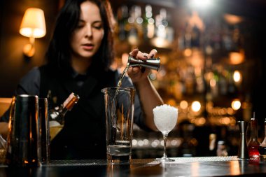 Barmen kız şeffaf bir alkollü içeceği zencefilden profesyonel bir çeliğe dolduruyor.