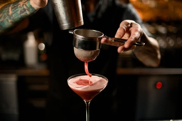 Bartender pouring a alcoholic drink from the steel shaker to the glass through the sieve — Stockfoto