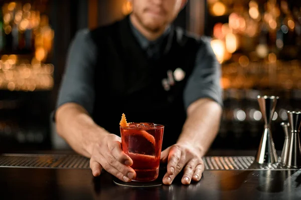 Barman servíruje červený alkoholický nápoj zdobený spirálovitě oranžovou kůrou a ledem — Stock fotografie