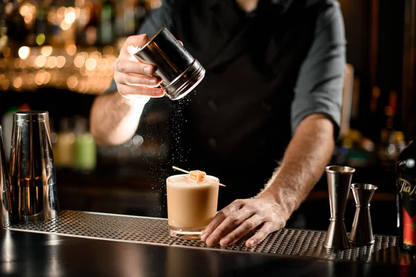 Barman serwujący kremowy napój alkoholowy ozdobiony cukierkami na szpikulcu posypującym go cukrem w proszku — Zdjęcie stockowe