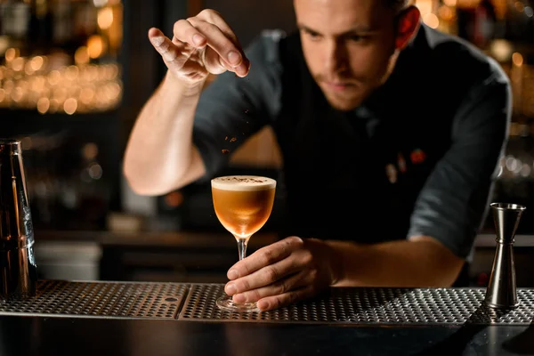 Barista maschio che serve la bevanda alcolica marrone cospargendola di spezie — Foto Stock