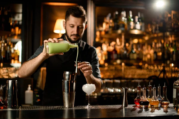 Man barman gieten een pistache kleur liqour van de glazen fles naar de stalen jigger — Stockfoto