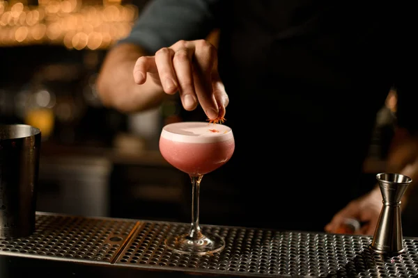 Professionele mannelijke barman serveert de roze alcoholische drank versierd met gele bloemblaadjes — Stockfoto