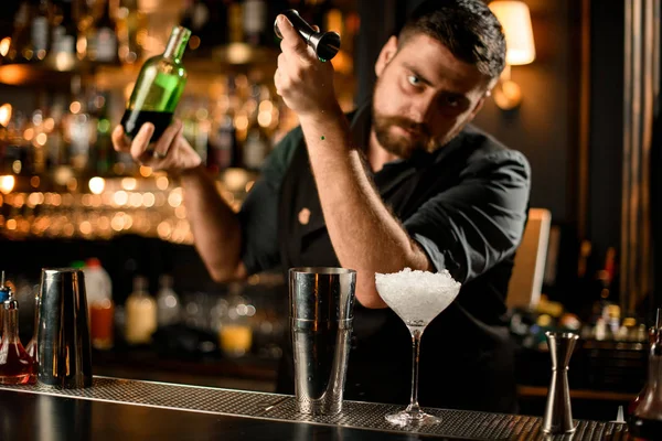 Barman masculino derramando um licor de cor verde do jigger para uma coqueteleira de aço profissional — Fotografia de Stock