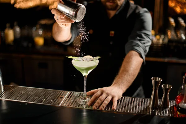 Barman que serve o coquetel de cor cremosa verde decorado com uma folha e laranja seca polvilhando-o com açúcar em pó — Fotografia de Stock